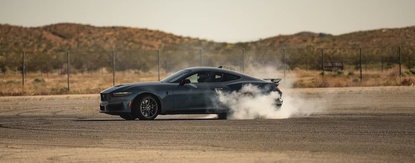 A black 2024 Ford Mustang performing a burnout.