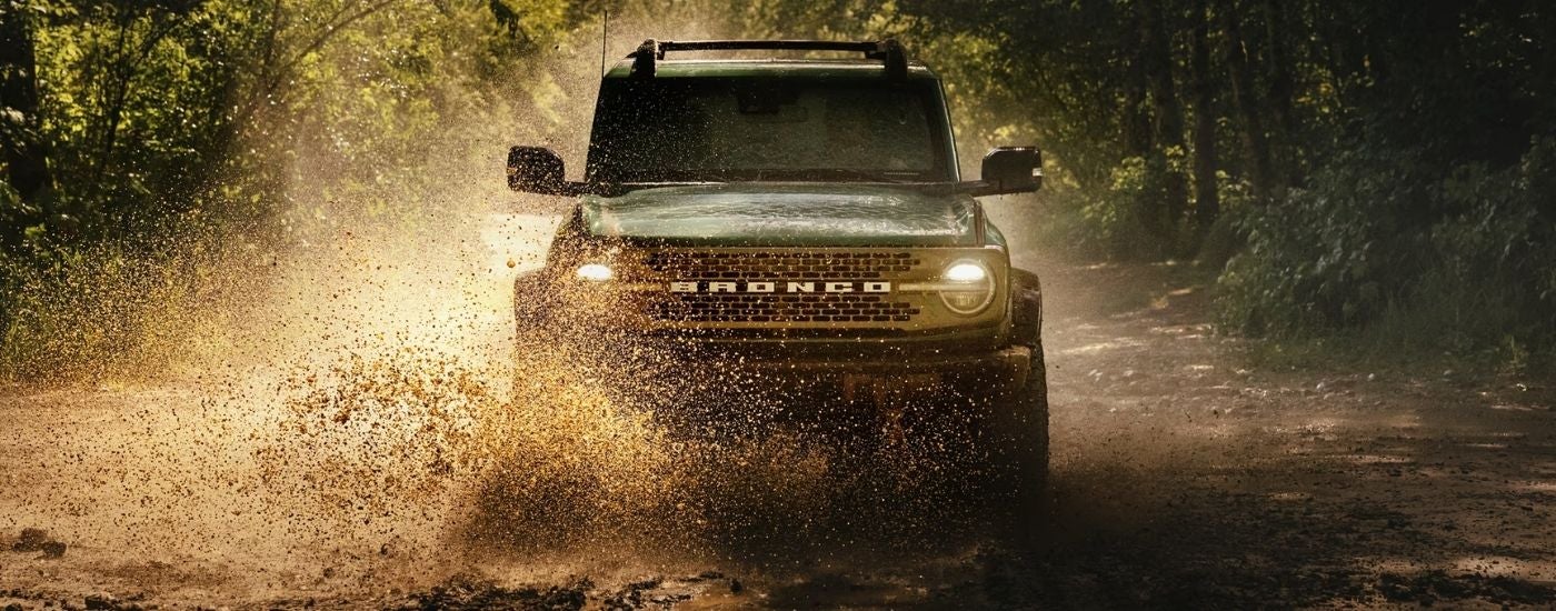 A black 2025 Ford Bronco off-roading in mud.