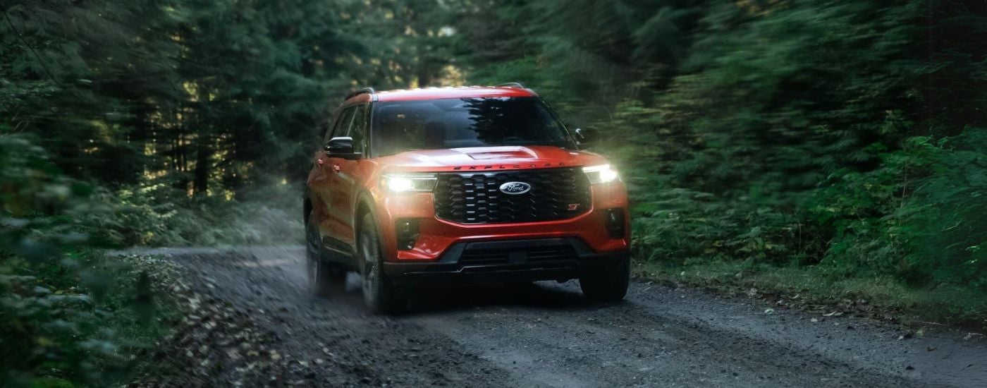 Red 2025 Ford Explorer ST driving off-road down a road.
