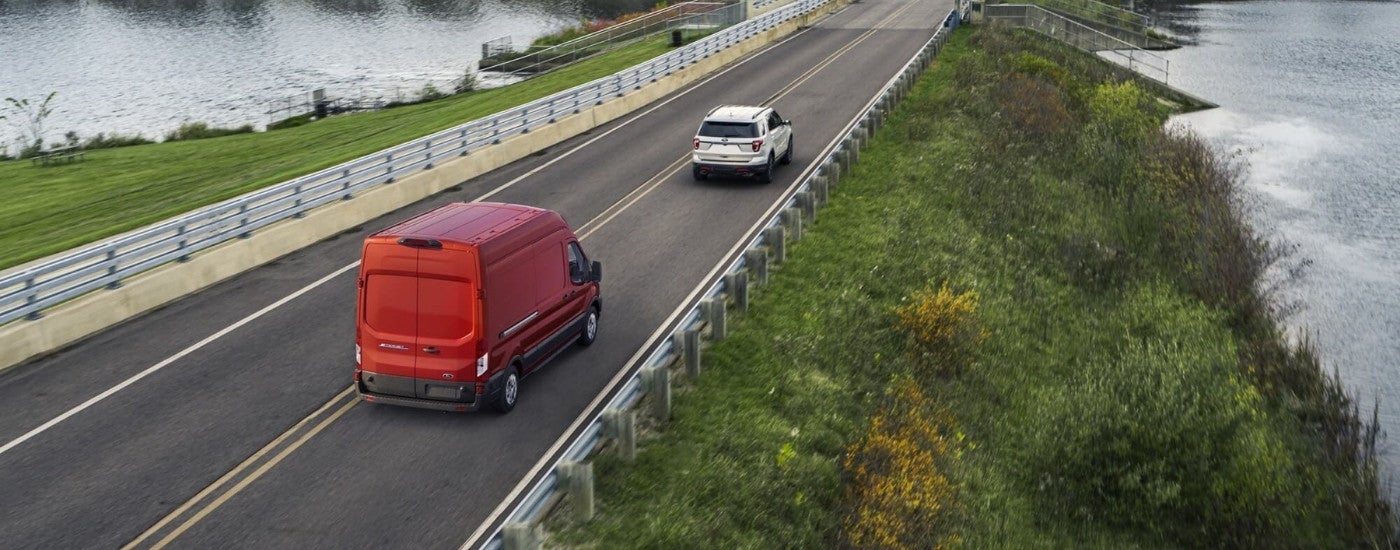 A red 2023 Ford E-Transit driving to a Ford dealer.